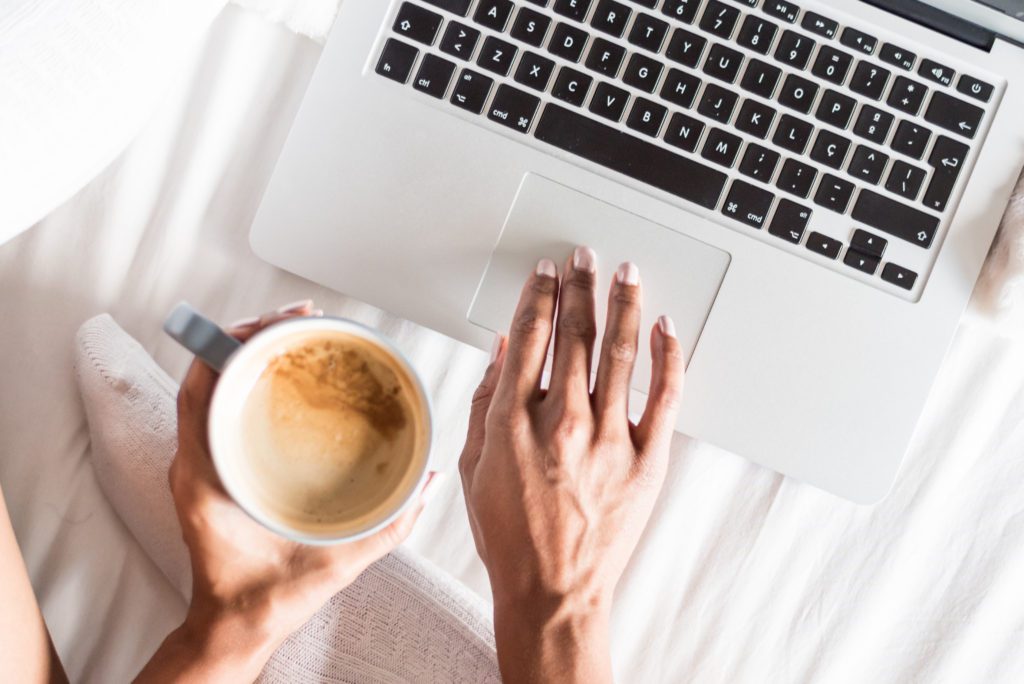 General photo of person typing on a laptop while holding coffee