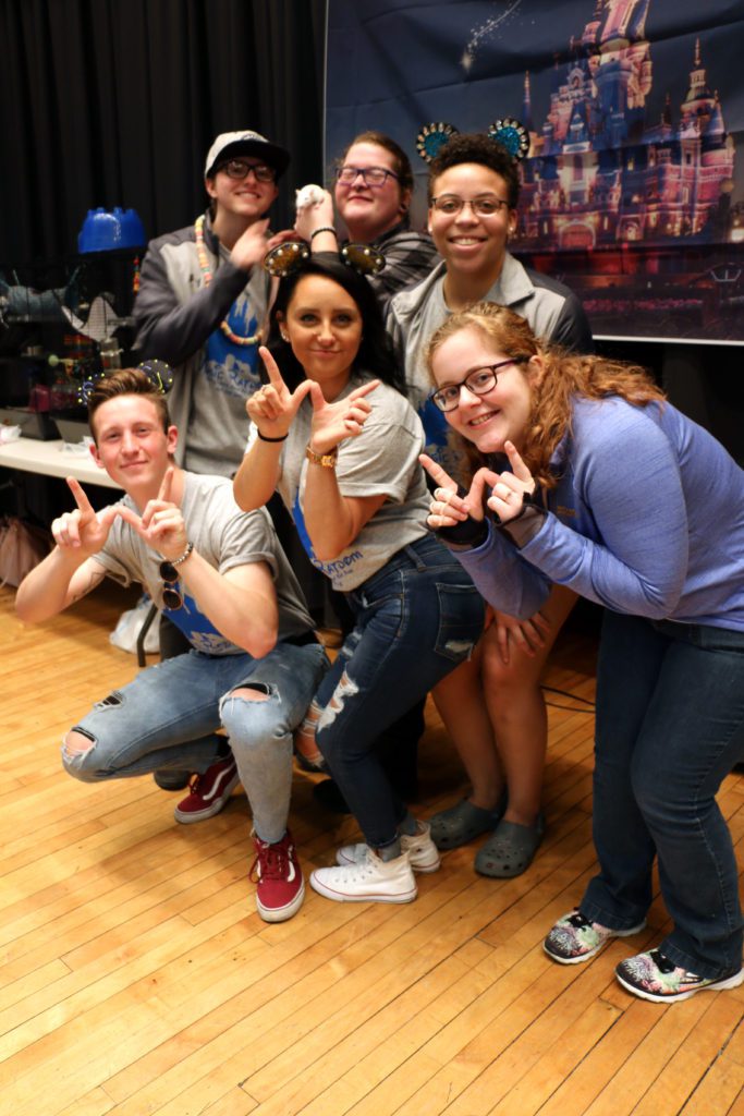 Group of smiling students, including one holding a white rat, making a 'W" gesture to celebrate Running of the Rodents victory