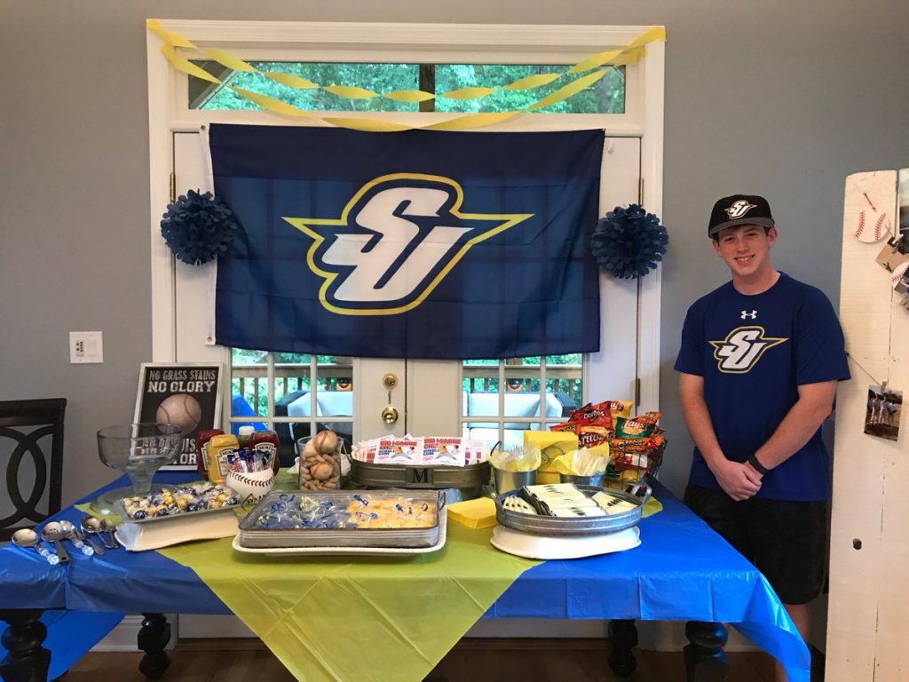 young man wearing Spalding T-shirt and ball cap next to a blue-and-gold party table with snacks and a Spalding flag behind it