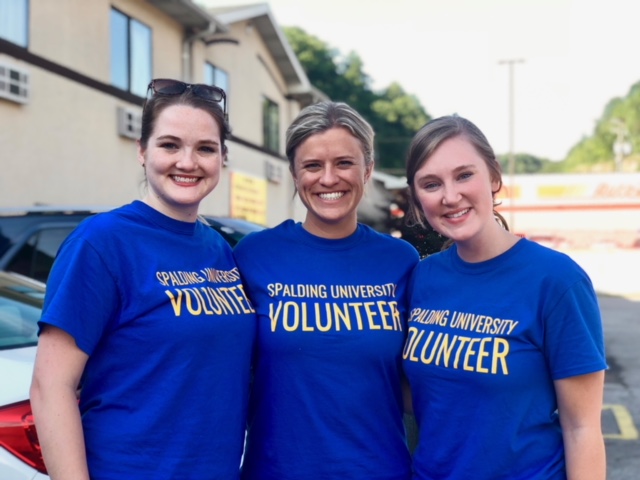 Three smiling women, wearing blue T-shirts that say "Spalding University Volunteers"
