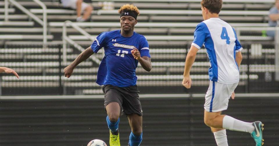 Spalding's Kornell Hilliard, in blue uniform, kicks a soccer ball past a defender in a white uniform