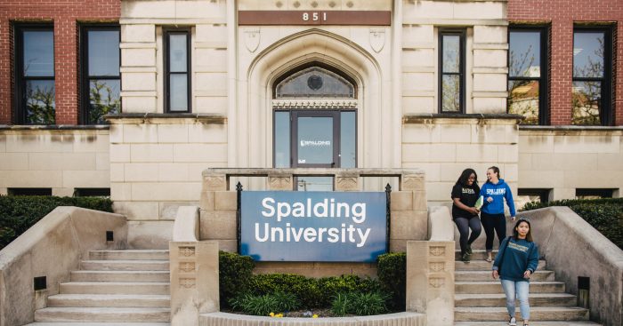 Front entrance to the Spalding Mansion with a blue "Spalding University" and three female students walking down the steps
