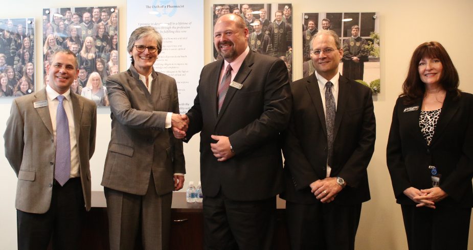 Spalding University President Tori Murden McClure and Sullivan University President Jay Marr shake hands, flanked by other administrators