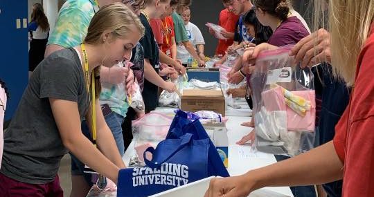 Spalding students at a long table pack hygiene kits that would be distributed to Wellspring clients